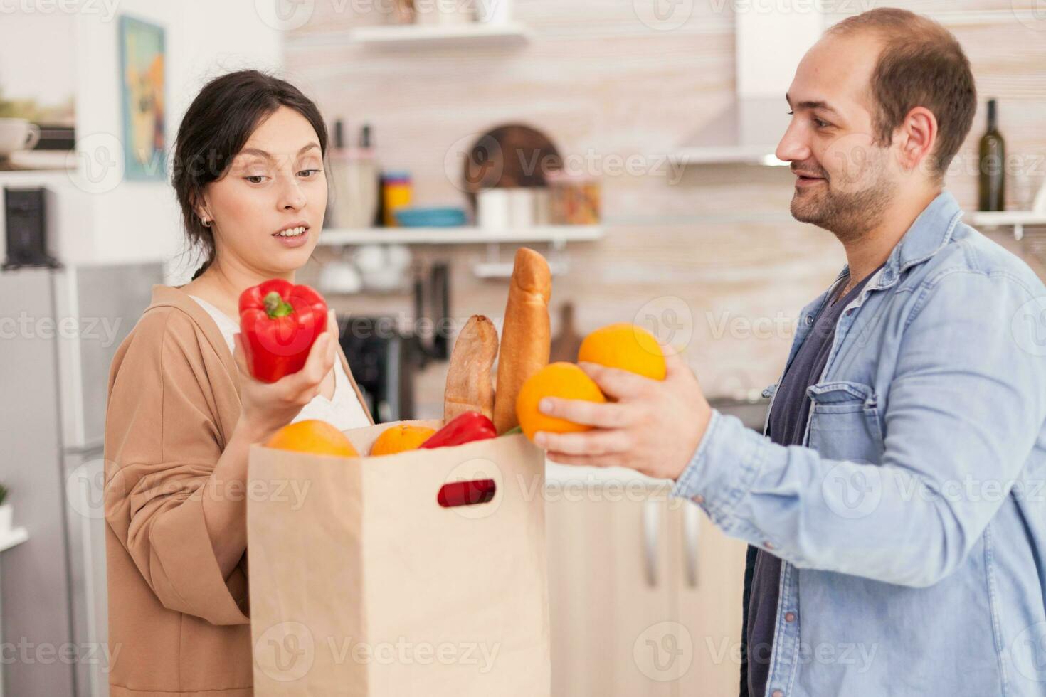 paar nemen uit vers groenten van papier zak in keuken na aankomen huis van supermarkt. gezond gelukkig verhouding levensstijl voor Mens en vrouw, samen boodschappen doen producten foto