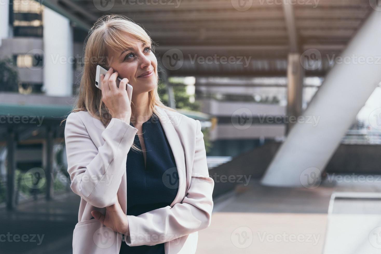 gelukkige zakenvrouw die slimme telefoon gebruikt om te communiceren en te praten met een zakelijke overeenkomst op de achtergrond van de stedelijke stad. mensen levensstijl en technologie concept. buiten werken en social distancing concept foto