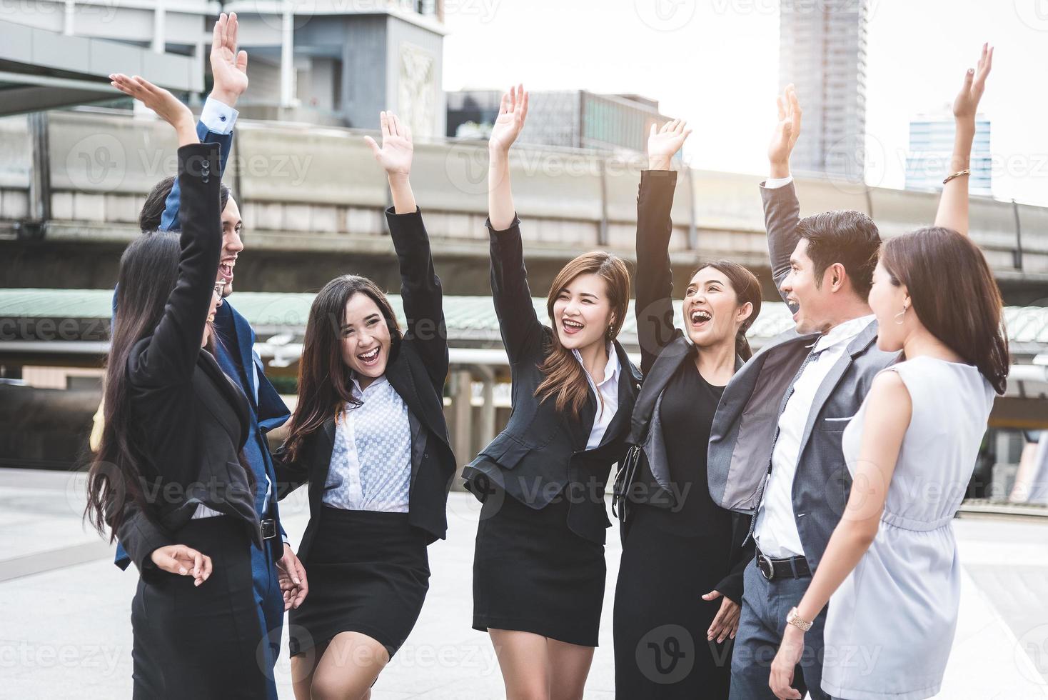 portret van een succesvolle groep zakenmensen in de buitenlucht. gelukkige zakenlieden en zakenvrouwen die hand opsteken als team in tevredenheidsgebaar. succesvolle groep mensen die lacht na prestatie foto