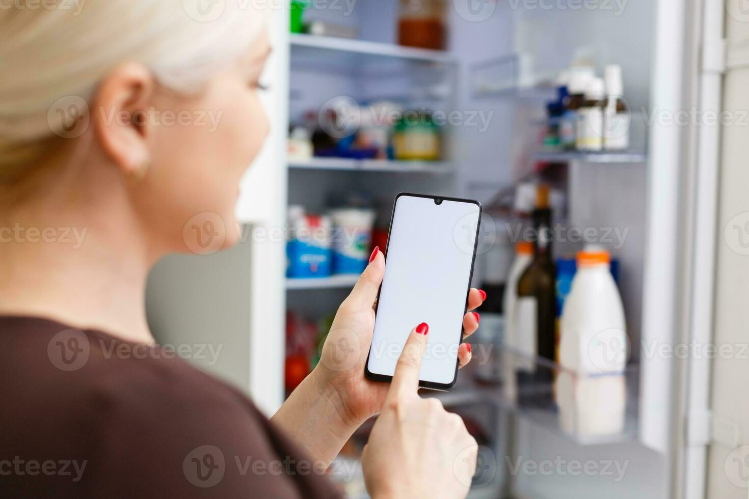 detailopname van vrouw hand- gebruik makend van energie etiket Aan mobiel telefoon tegen koelkast Bij huis foto