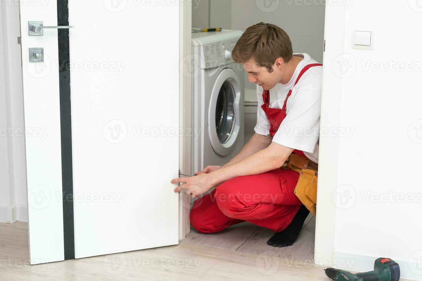 installatie van een slot Aan de voorkant houten Ingang deur. portret van jong slotenmaker werkman in blauw uniform installeren deur knop. professioneel reparatie onderhoud. onderhoud concept foto