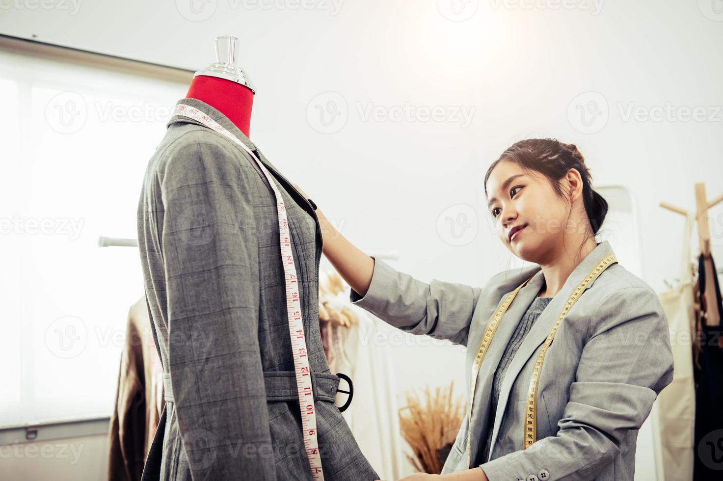 Aziatische vrouwelijke modeontwerper meisje passen op de formele pak uniforme kleding op mannequin model. modeontwerper stijlvolle showroom. naai- en kleermakersconcept. creatieve naaister stylist foto