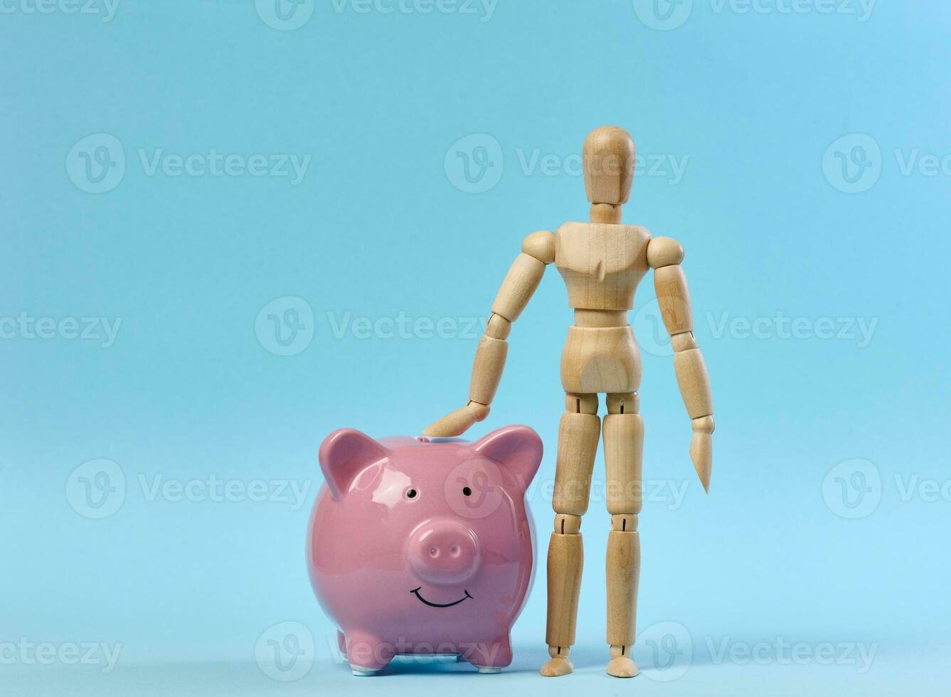 keramisch roze varkentje bank en een houten marionet pop Aan een blauw achtergrond. concept van toenemend inkomen van bank rekeningen foto