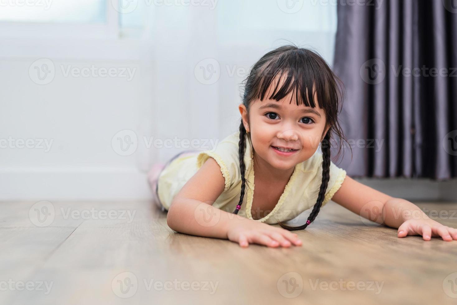 portret van een schattig klein meisje dat met blote voeten op de vloer ligt en thuis naar de camera kijkt. mensen levensstijl concept foto