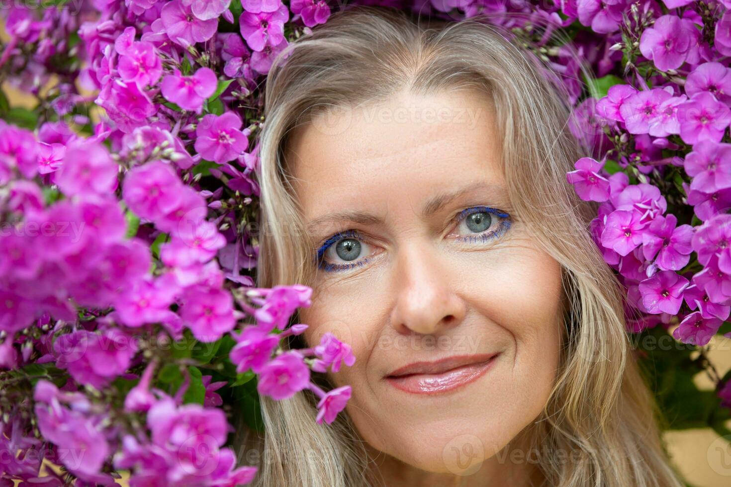 portret van een mooi midden- oud blond vrouw omringd door Purper bloemen. aantrekkelijk ouderen vrouw gezicht. foto