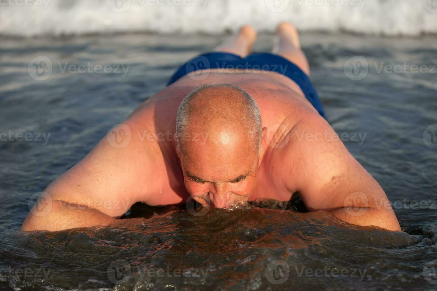 een ouderen Mens leugens in de zee water, geniet de rust uit. foto