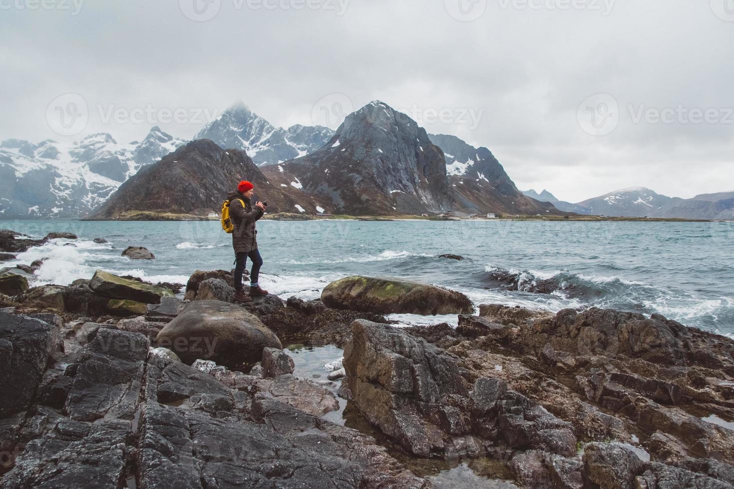 reizigersfotograaf die natuurfoto maakt die op rotsen staat tegen de achtergrond van de zee en de bergen foto