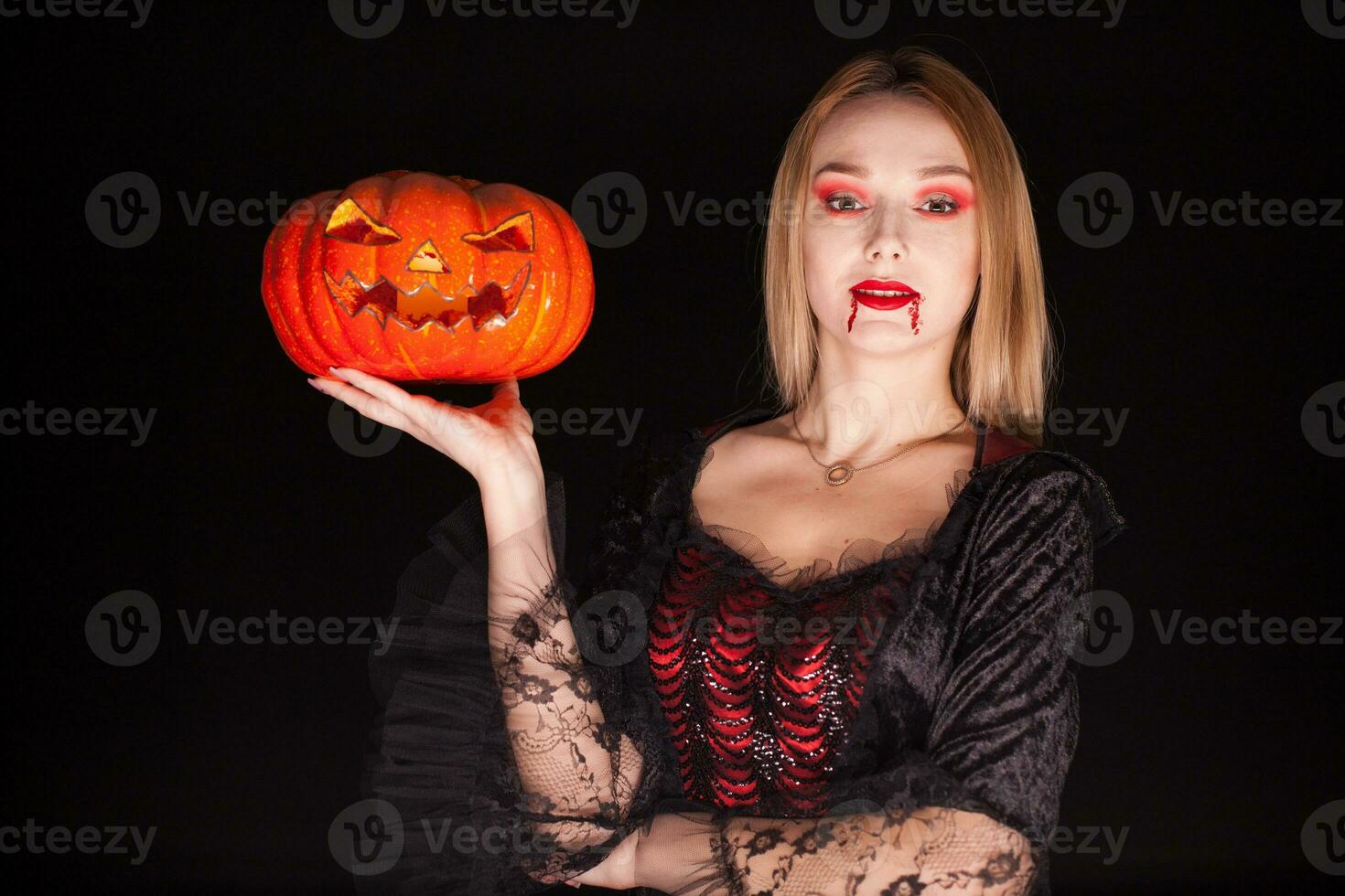 mooi blond vrouw gekleed omhoog Leuk vinden een onheil vampier Holding een pompoen voor halloween. foto