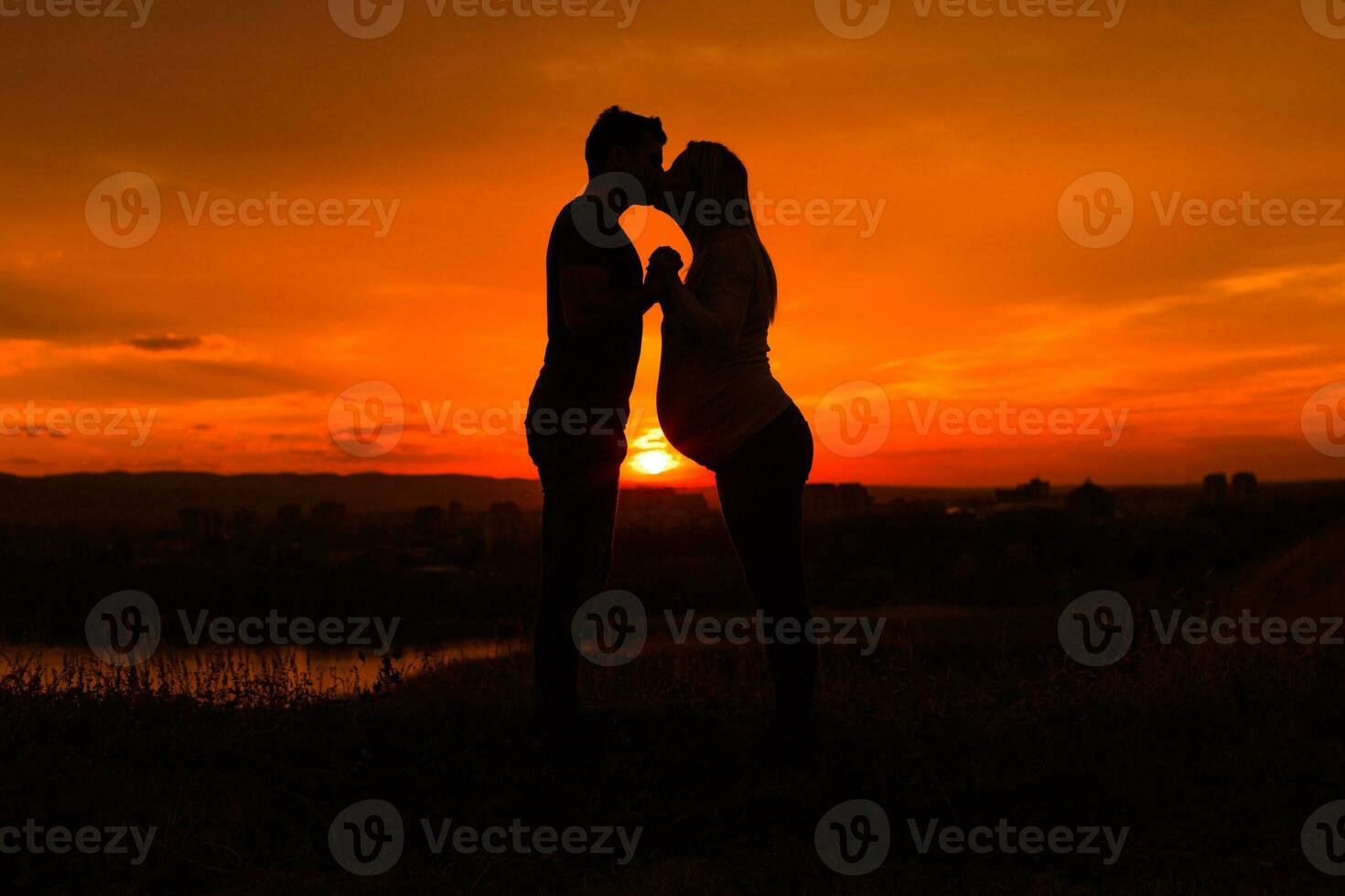 silhouetten van man en zwanger vrouw zoenen terwijl ze genieten uitgeven tijd samen buiten.afgezwakt afbeelding. foto