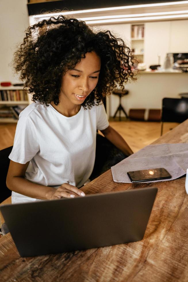 zwarte jonge vrouw die met laptop werkt terwijl ze aan tafel zit foto