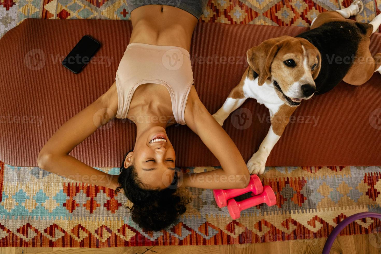 zwarte jonge vrouw die lacht terwijl ze met haar hond op de mat ligt foto