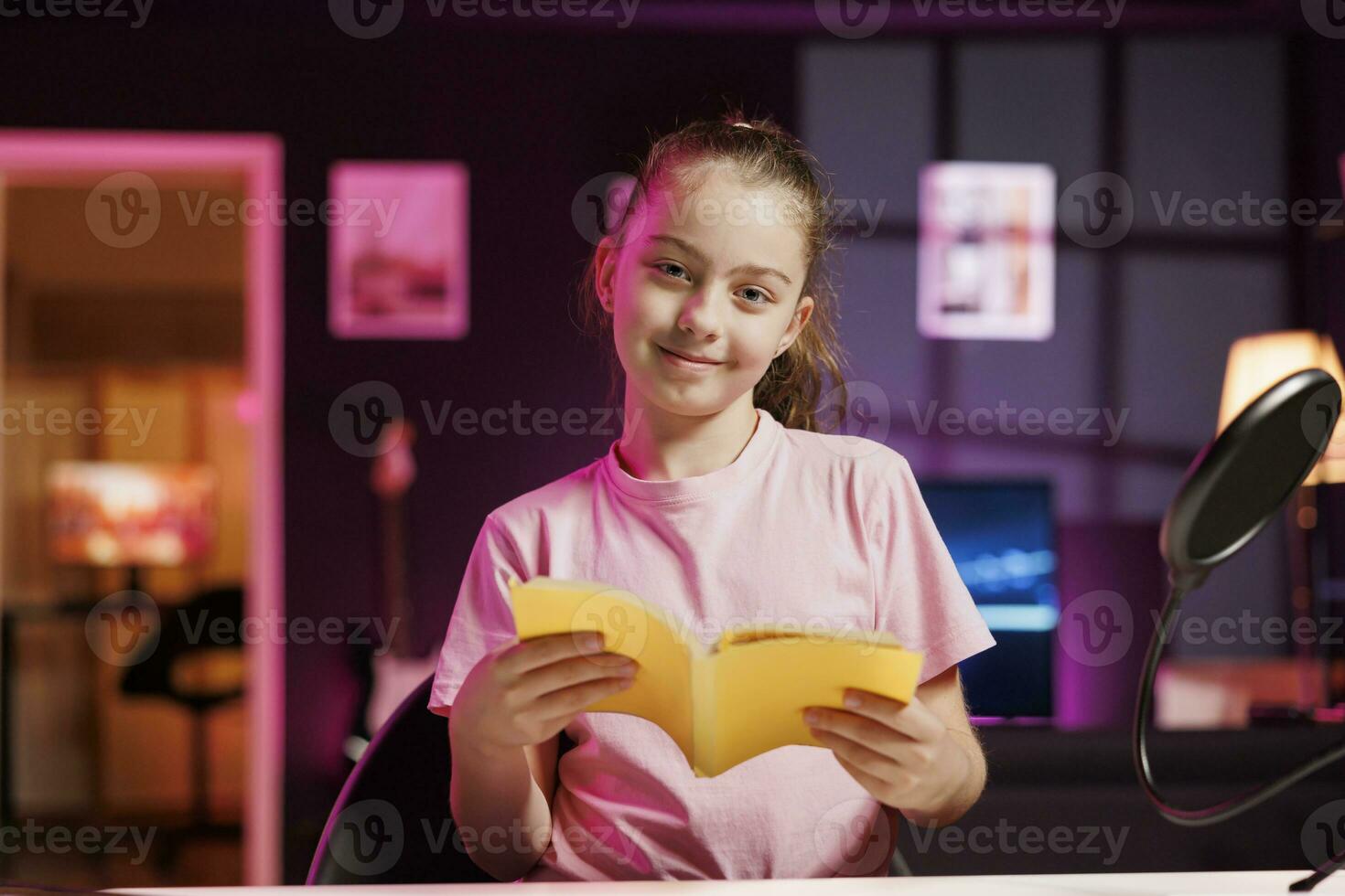 kind influencer in studio lezing nieuw vrijgelaten hardcover boek van uitgever. schattig meisje filmen literatuur video essay, presenteren nieuw roman van auteur naar lezers in roze neon lit studio foto