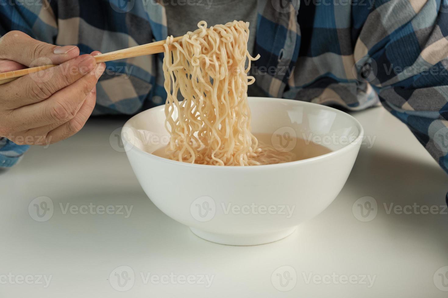 hongerige casual thaise man gebruikt eetstokjes om hete instantnoedels in een witte kop te eten tijdens lunchpauzes, snel, smakelijk en goedkoop. traditionele gezonde Aziatische fastfoodmaaltijd van Japanse en Chinese levensstijl. foto