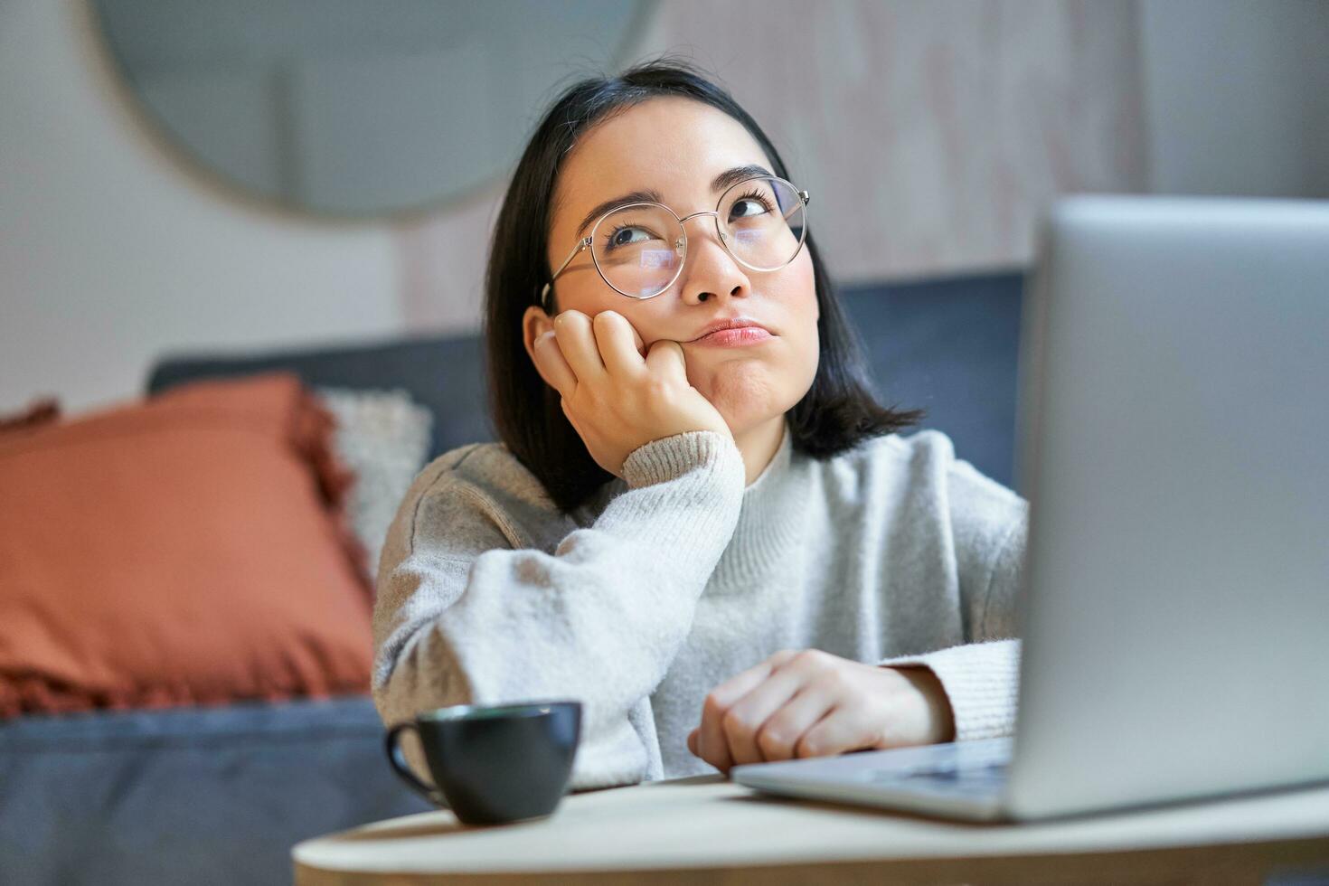 portret van Koreaans meisje zit verveeld, leerling looks somber Bij laptop, zittend Bij huis en uitdrukken verveling foto