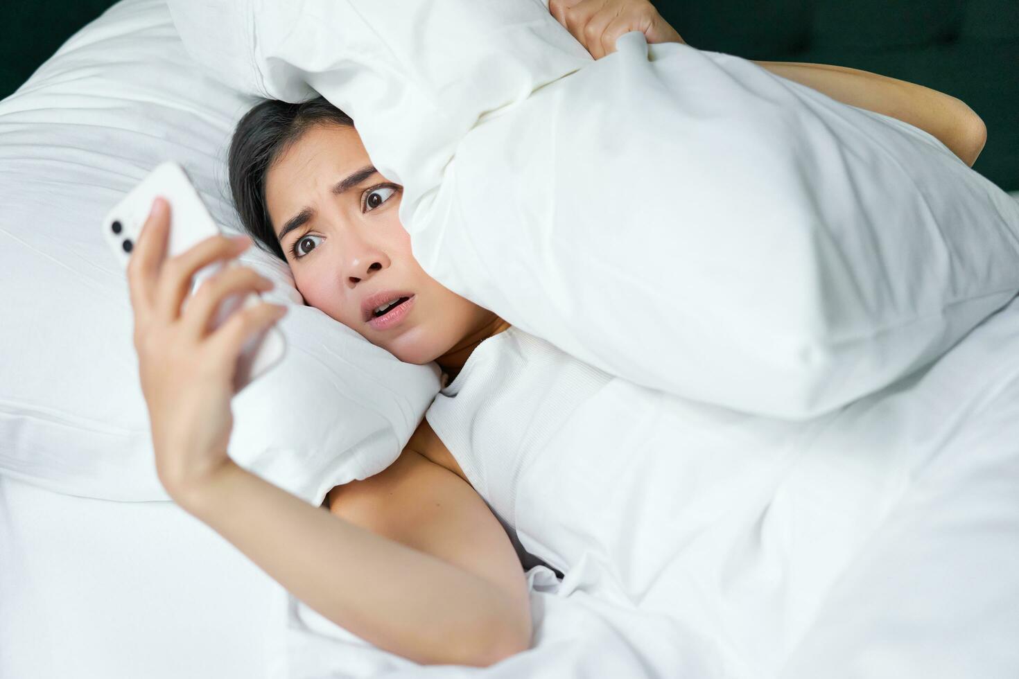 portret van Aziatisch vrouw ontwaken omhoog in bed, op zoek geschokt Bij mobiel telefoon, realiseren ze verslapen foto