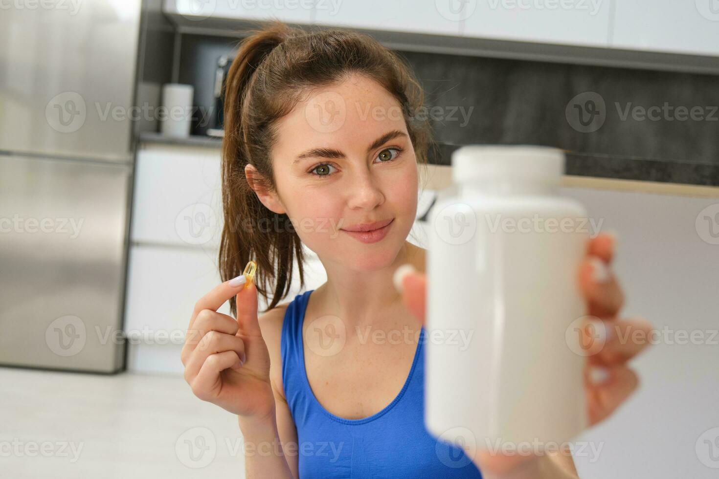 dichtbij omhoog portret van geschiktheid vrouw, meisje training van huis, tonen fles van vitamines, dieet supplement pillen, aanbevelen bloemknoppen foto