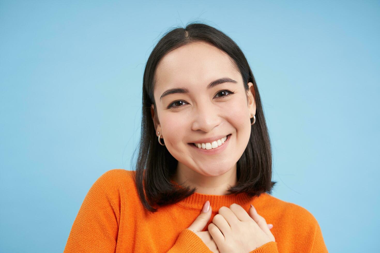 dichtbij omhoog portret van Aziatisch meisje met perfect gezond glimlach en natuurlijk mooi gezicht, looks gelukkig Bij camera, staat over- blauw achtergrond foto