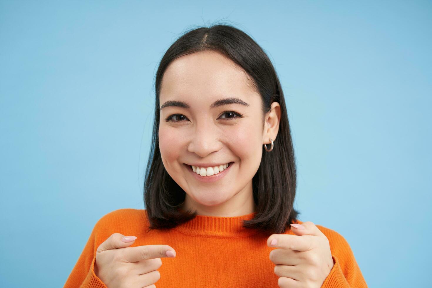 heb je. dichtbij omhoog portret van glimlachen Aziatisch vrouw points vingers Bij camera verheugd, feliciteert jij, staat over- blauw achtergrond foto