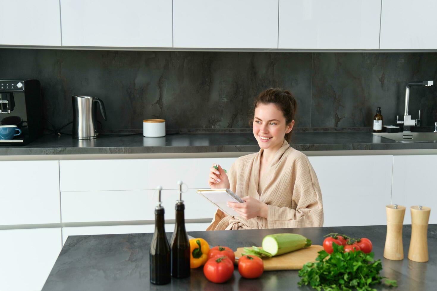 portret van vrouw schrijven naar beneden lijst van boodschappen, maken aantekeningen in recept, zittend in keuken in de buurt groenten, voorbereidingen treffen avondeten menu foto