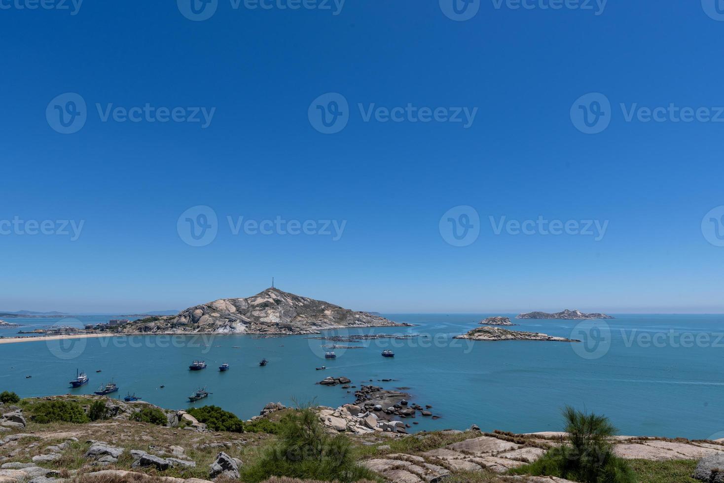 sta hoog en kijk naar het zeelandschap onder de blauwe lucht, blauw water, witte golven en zwarte rotsen foto