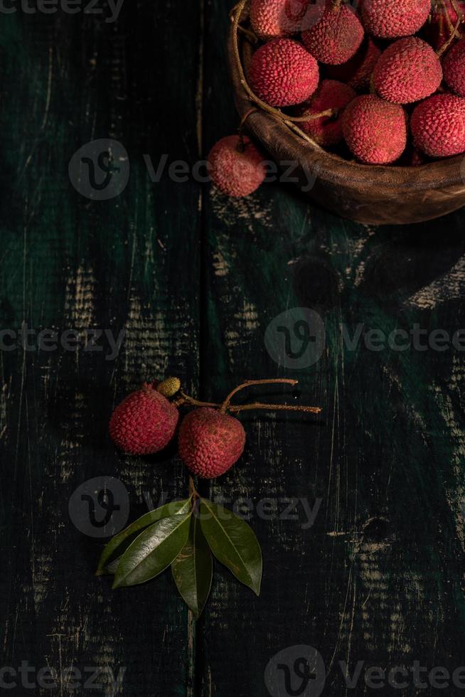 lychee wordt in een houten bord geplaatst, geschild of ongeopend, op een donkere houtnerftafel foto