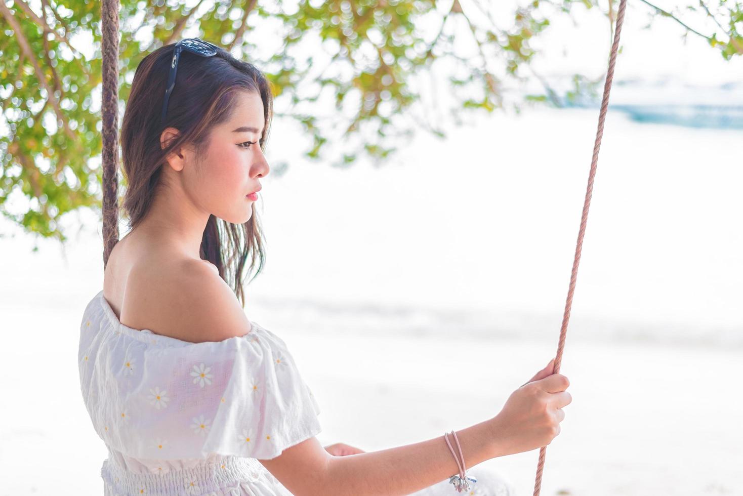 Aziatische vrouw op witte jurk zittend op de schommel op het strand. mensen en natuur concept. trieste liefde en iemand missen concept. eenzaam en gebroken hart thema foto