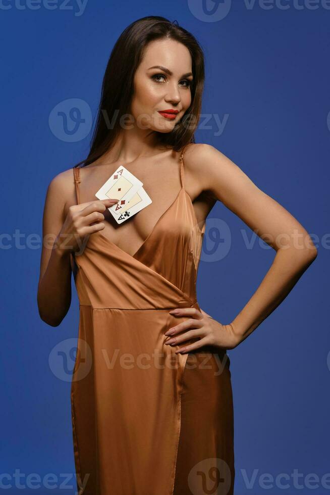 brunette meisje in zijde gouden jurk. ze lachend, tonen twee azen, poseren tegen blauw achtergrond. gokken, poker, casino. detailopname foto