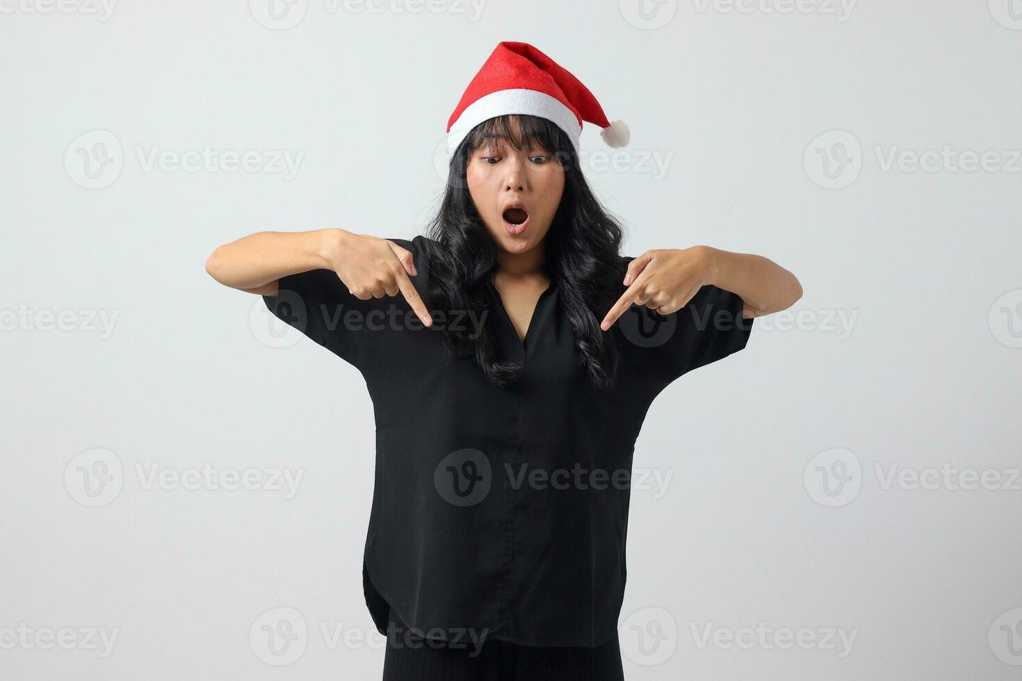 portret van aantrekkelijk Aziatisch vrouw met rood de kerstman hoed gevoel Vrolijk, tonen en richten naar beneden met vinger. nieuw jaar en Kerstmis concept. geïsoleerd beeld Aan wit achtergrond foto