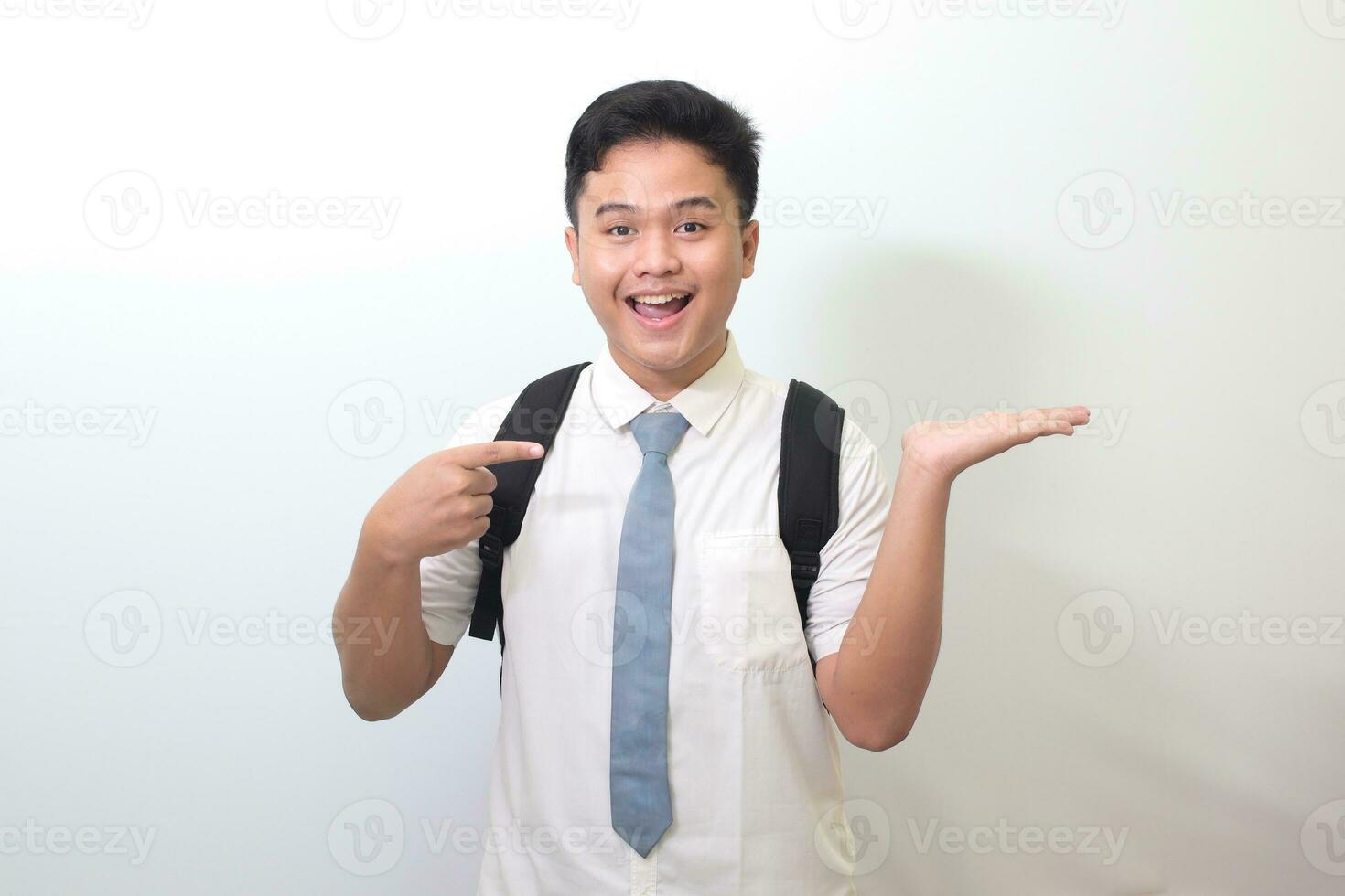 Indonesisch senior hoog school- leerling vervelend wit overhemd uniform met grijs binden, glimlachen en op zoek Bij de camera, tonen iets met handen. geïsoleerd beeld Aan wit achtergrond foto