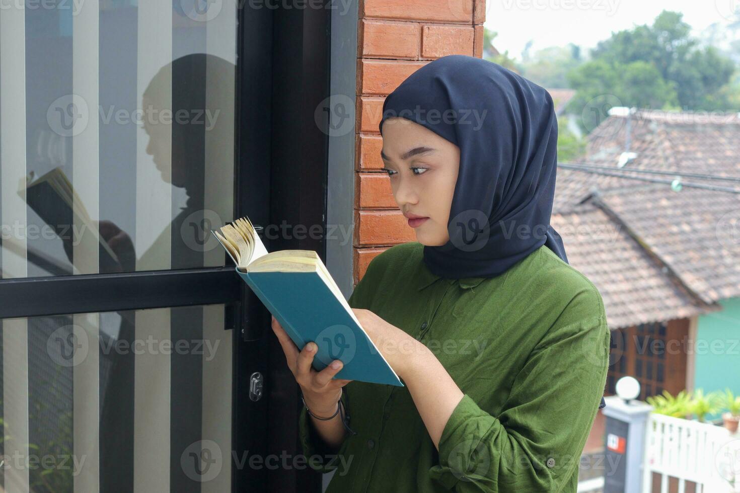 portret van aantrekkelijk Aziatisch hijab vrouw Holding boek in balkon. moslim meisje lezing een boek. concept van geletterdheid en kennis foto