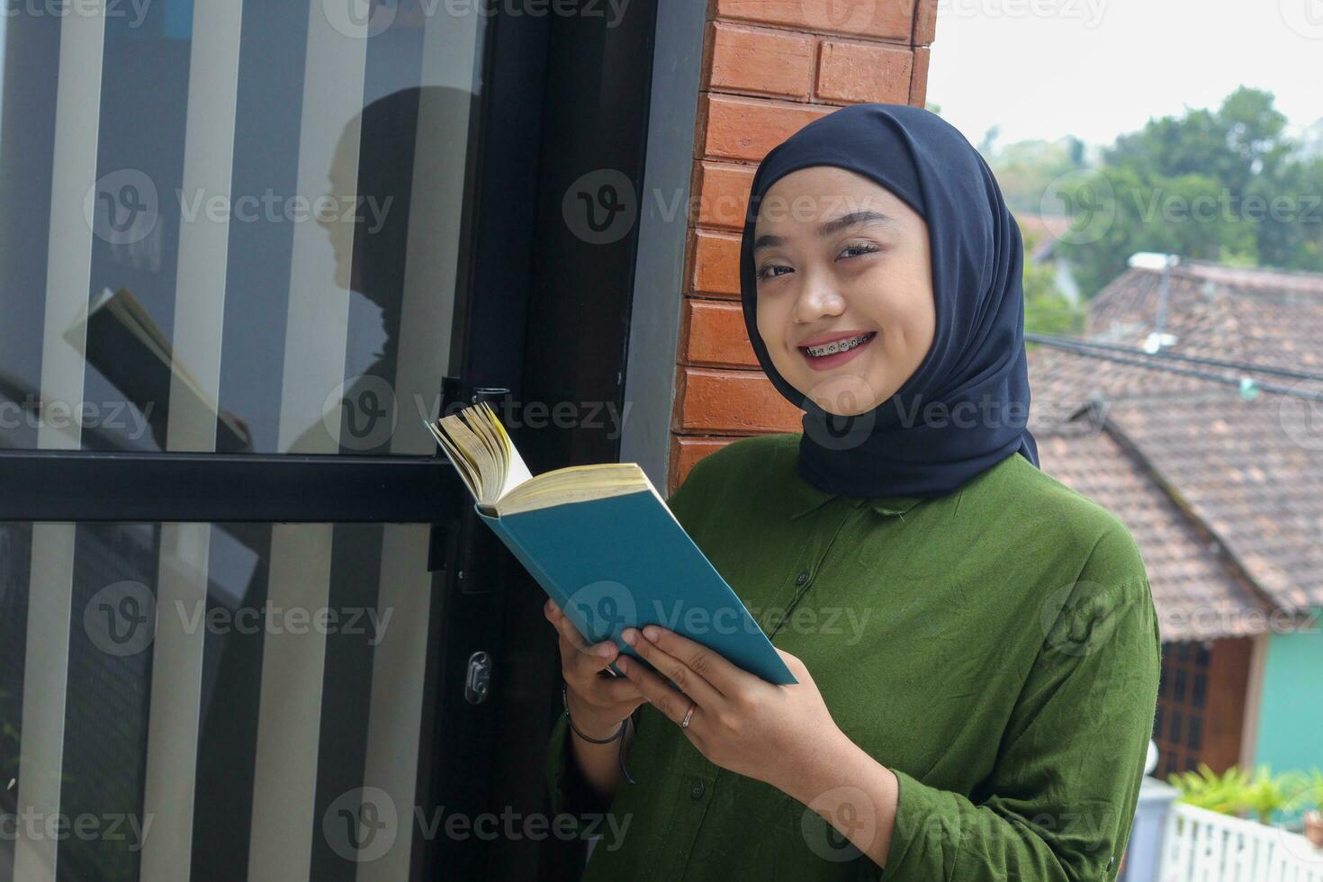 portret van aantrekkelijk Aziatisch hijab vrouw Holding boek in balkon. moslim meisje lezing een boek. concept van geletterdheid en kennis foto