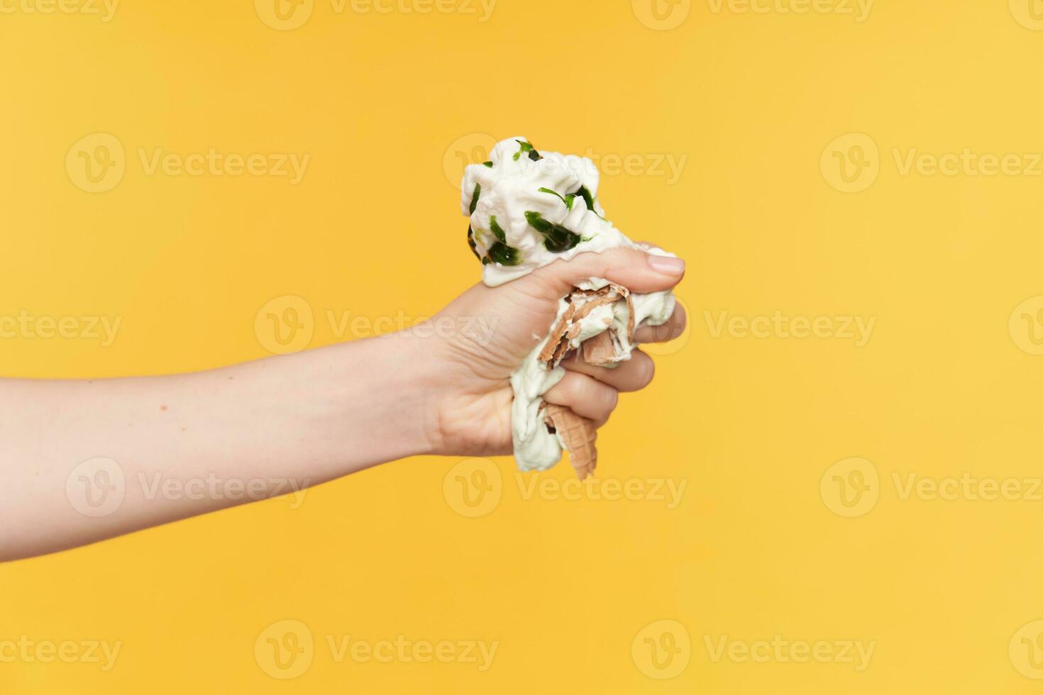 binnen- foto van lichte huid vrouw hand- met naakt manicure knijpen boos met vingers ijsje terwijl wezen geïsoleerd tegen geel achtergrond