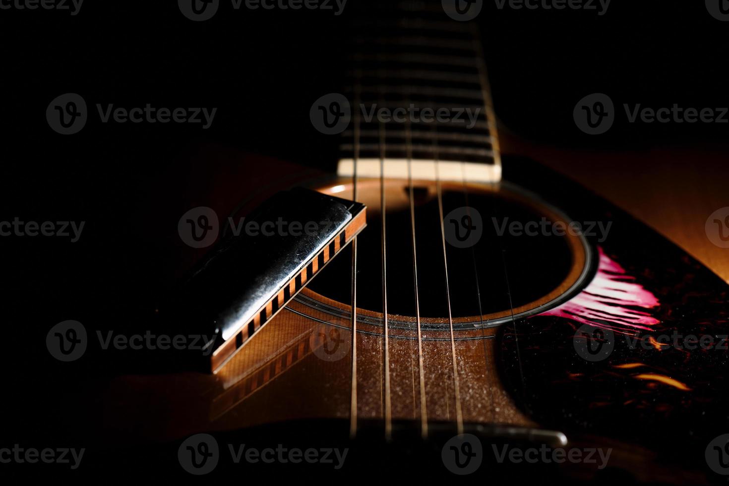 detail van een bluesharmonica bij het klankgat van een akoestische gitaar foto