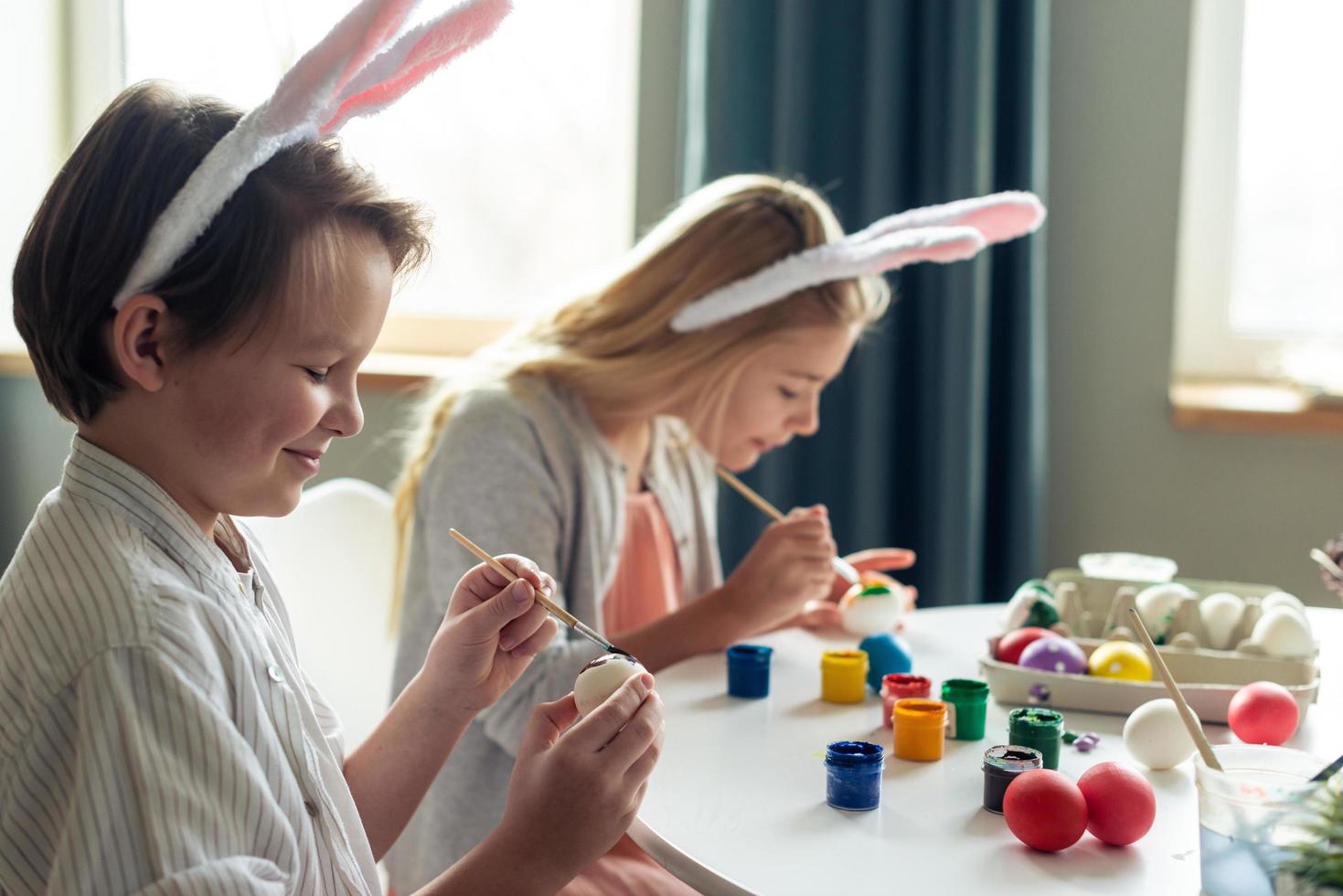 schattige, lachende kinderen schilderen zorgvuldig paaseieren met verf foto