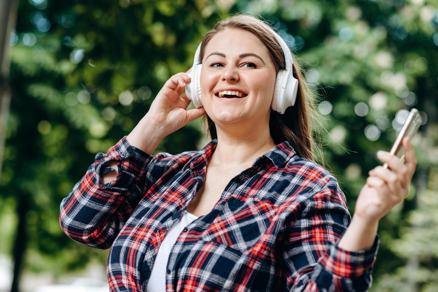 charmante, moderne vrouw in witte, draadloze koptelefoon die buiten plezier heeft foto