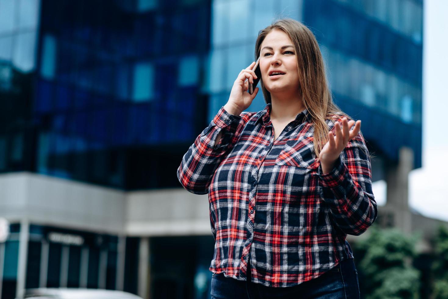 mooie, zakenvrouw in een geruit hemd communiceert aan de telefoon op de achtergrond van het zakencentrum foto