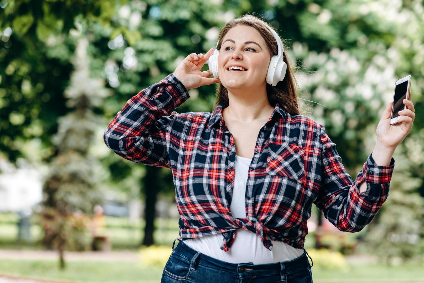 schattig, lachend, vrolijk meisje plus size, zingt haar favoriete liedje terwijl ze buiten loopt foto