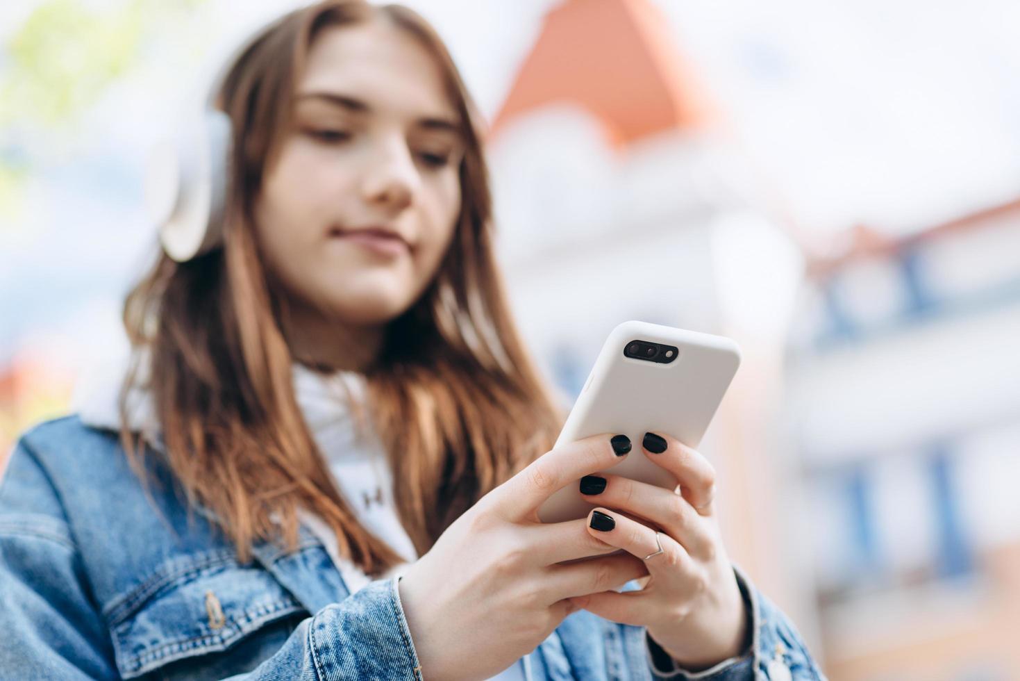 op een onscherpe achtergrond luistert een meisje naar muziek met een draadloze koptelefoon van een smartphone op straat. foto