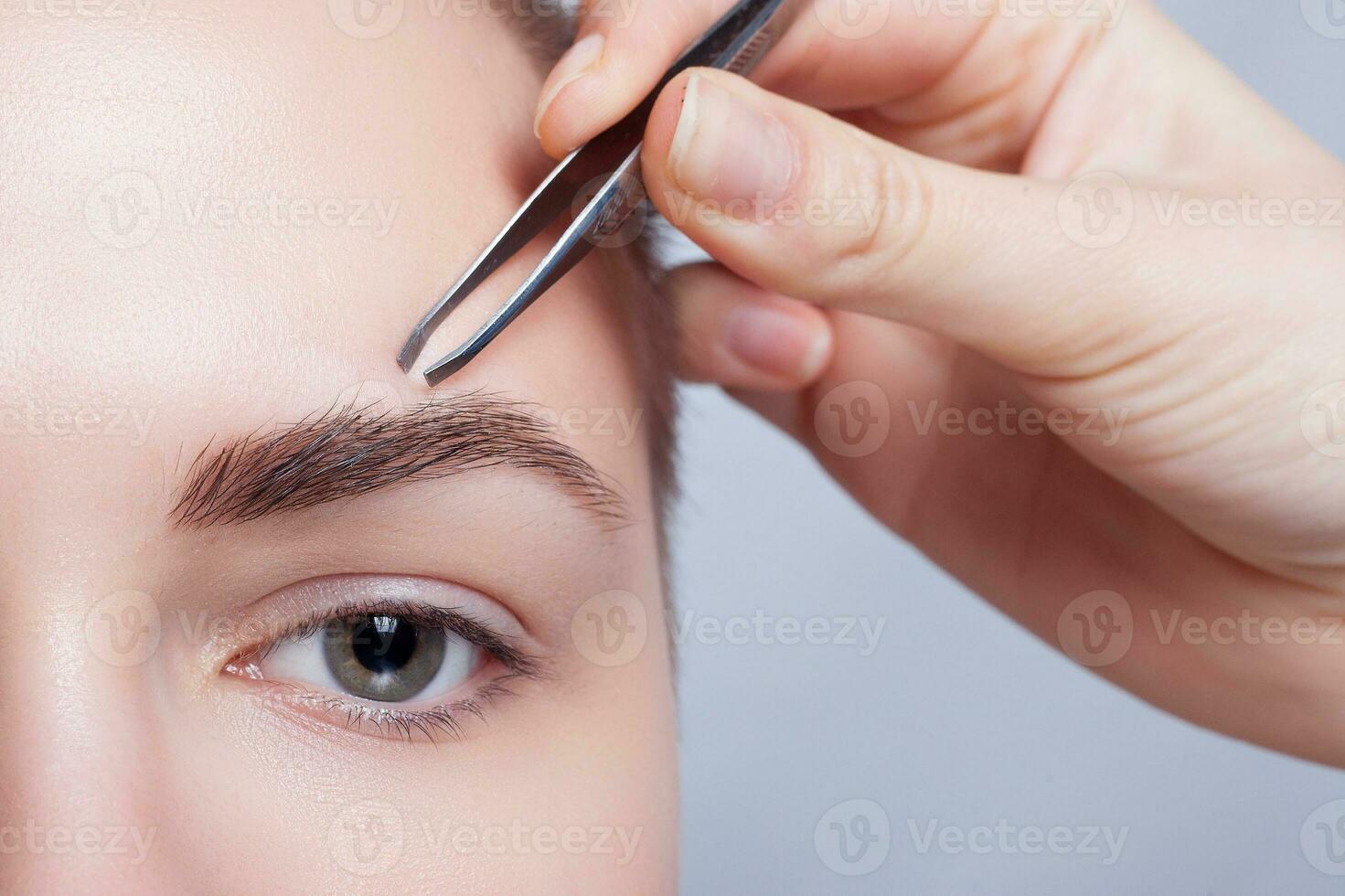 jong vrouw met kort haar- plukken wenkbrauwen pincet dichtbij omhoog foto