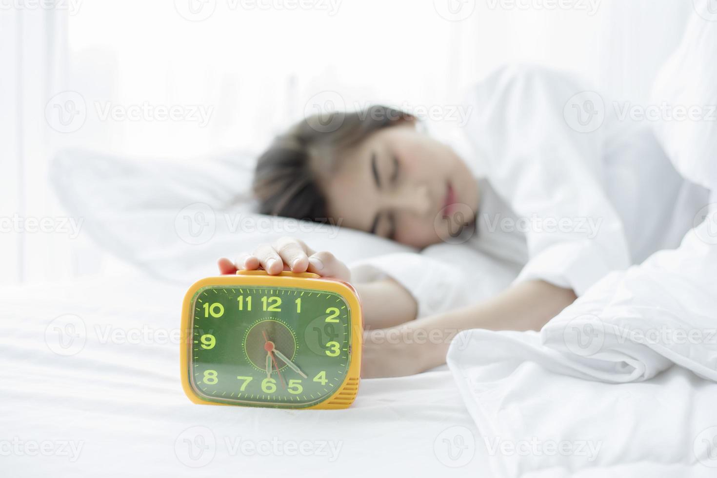 Aziatische vrouw blij wakker worden en de wekker uitzetten met een goede dag foto