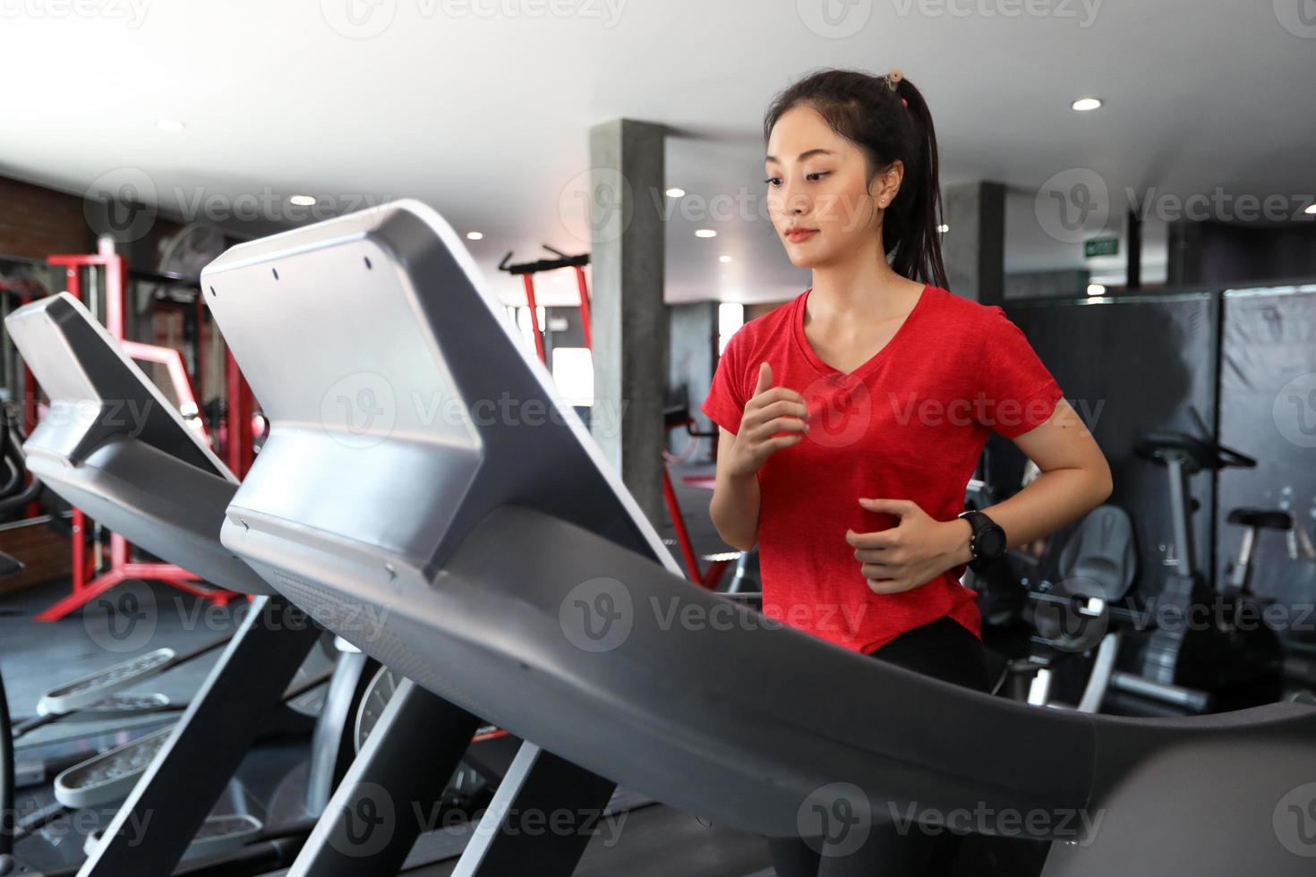 Aziatische vrouwen lopen sportschoenen in de sportschool terwijl een jonge blanke vrouw jogt op de loopband foto
