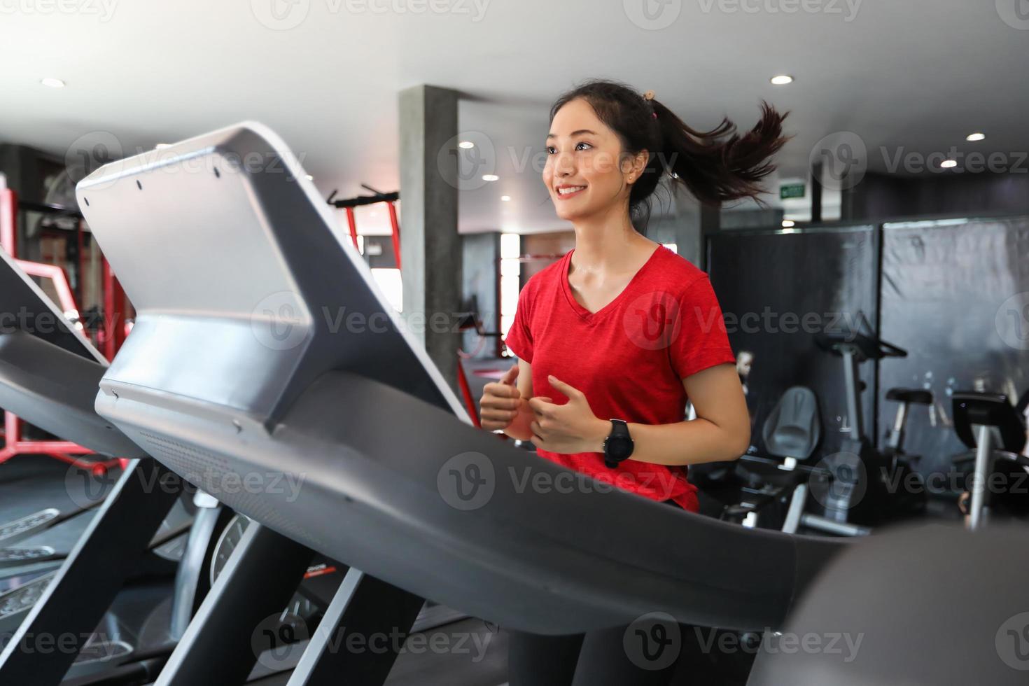 Aziatische vrouwen lopen sportschoenen in de sportschool terwijl een jonge blanke vrouw jogt op de loopband foto