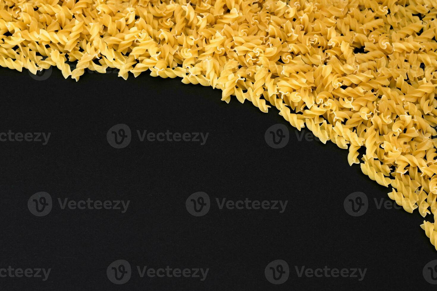 ongekookt fusilli pasta met kopiëren ruimte Aan zwart achtergrond. rauw en droog macaroni. dik en ongezond voedsel vlak leggen foto