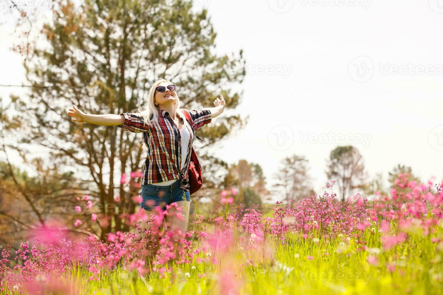 gelukkig avonturier vrouw staat Aan de groen berg helling tussen bloeiend roze rododendrons en op zoek in de afstand. episch reizen in de bergen. breed hoek. foto