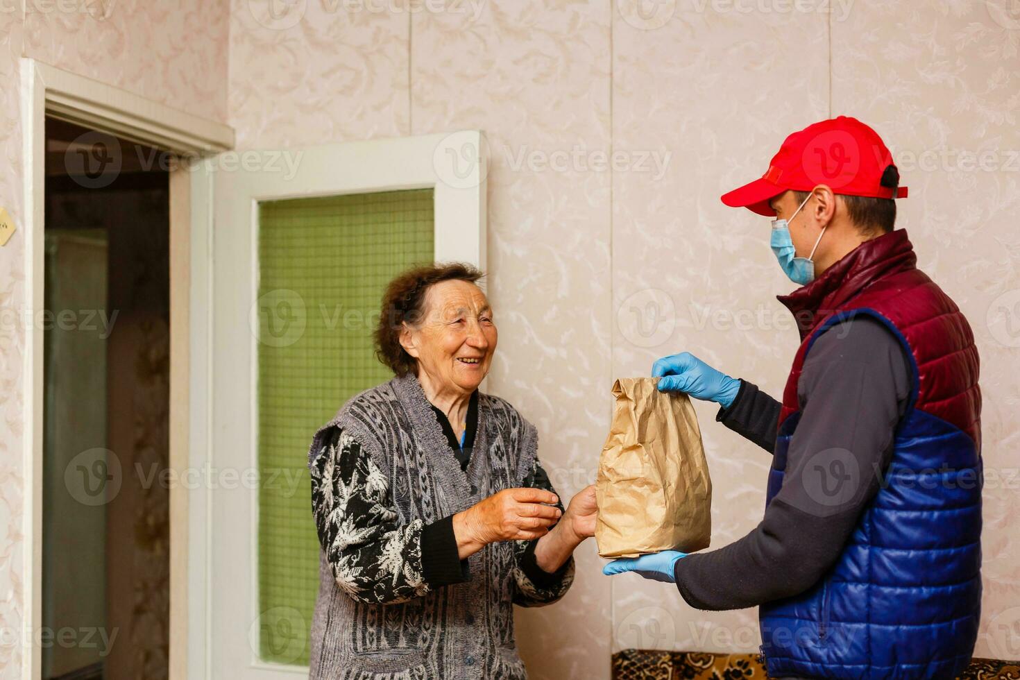 jong mannetje vrijwilliger in masker geeft een ouderen vrouw dozen met voedsel in de buurt haar huis. zoon Mens helpt een single ouderen moeder. familie steun, zorgzaam. in quarantaine geplaatst, geïsoleerd. coronavirus covid19. bijdrage foto