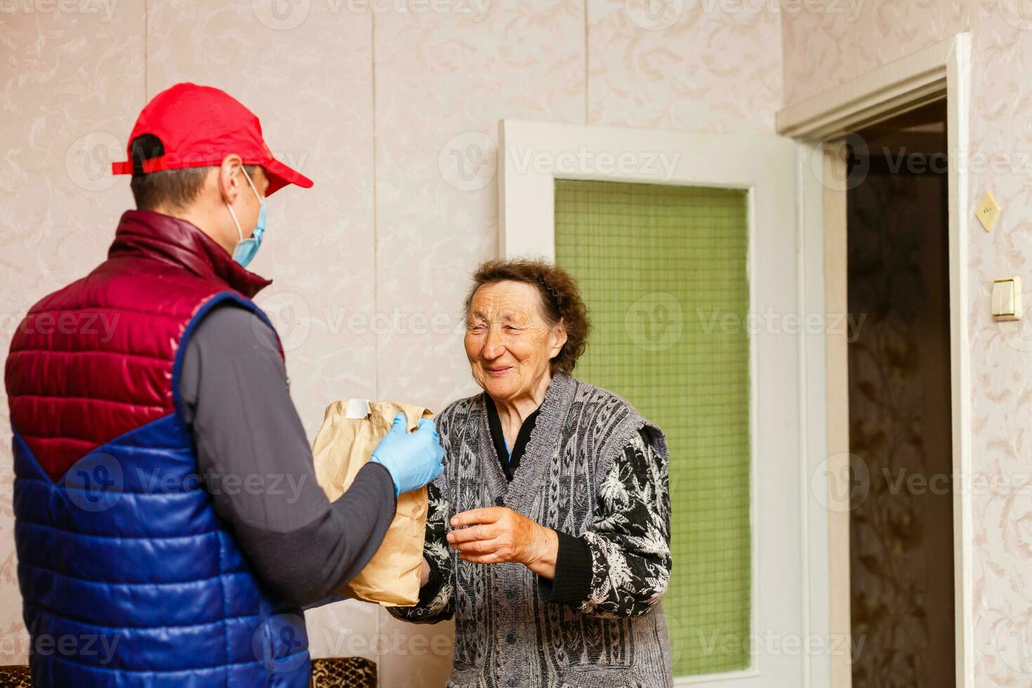 jong mannetje vrijwilliger in masker geeft een ouderen vrouw dozen met voedsel in de buurt haar huis. zoon Mens helpt een single ouderen moeder. familie steun, zorgzaam. in quarantaine geplaatst, geïsoleerd. coronavirus covid19. bijdrage foto