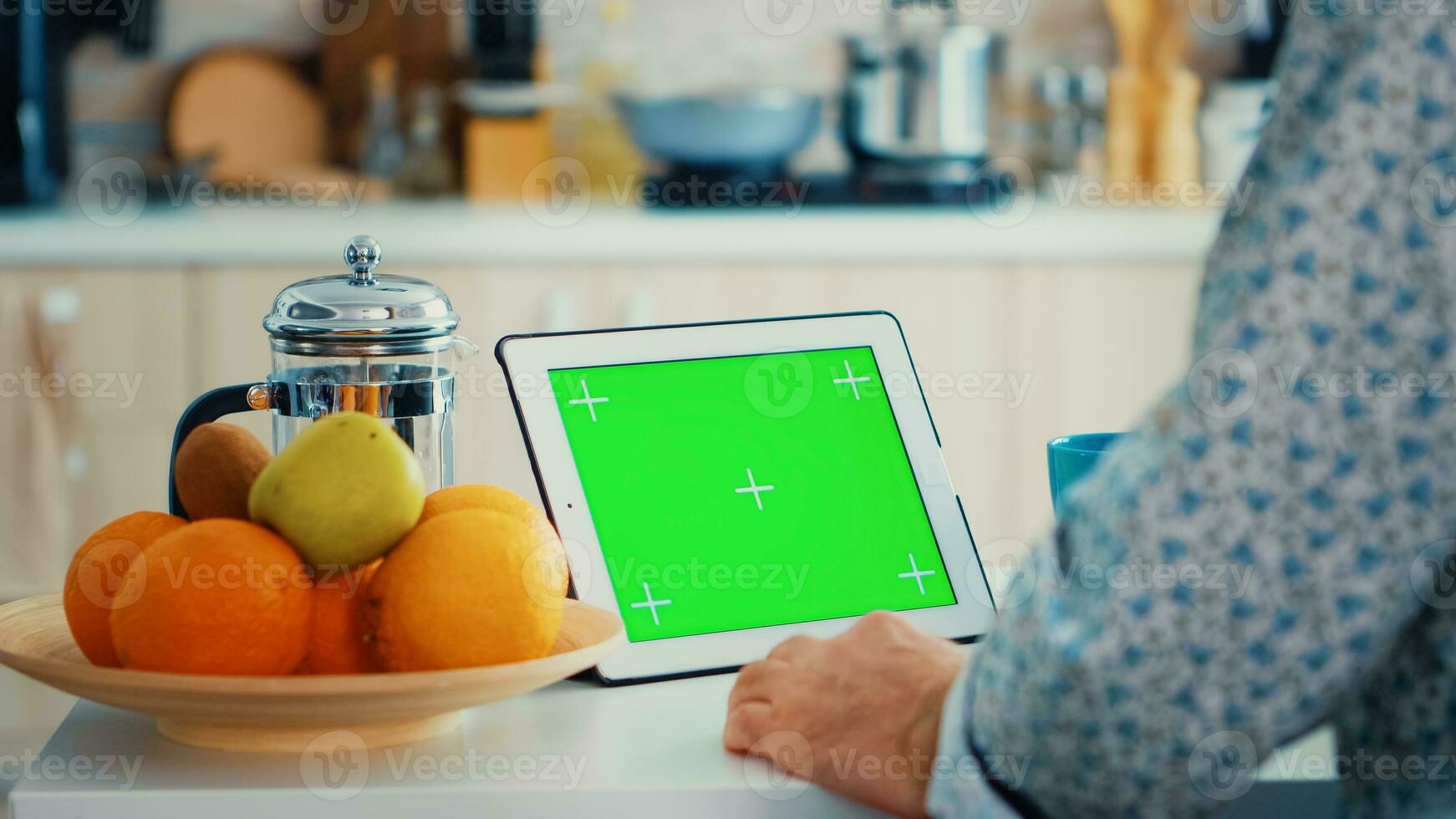 opa op zoek Bij tablet pc met groen scherm gedurende ontbijt in keuken. ouderen persoon met chroma sleutel geïsoleerd mockup mockup voor gemakkelijk vervanging foto