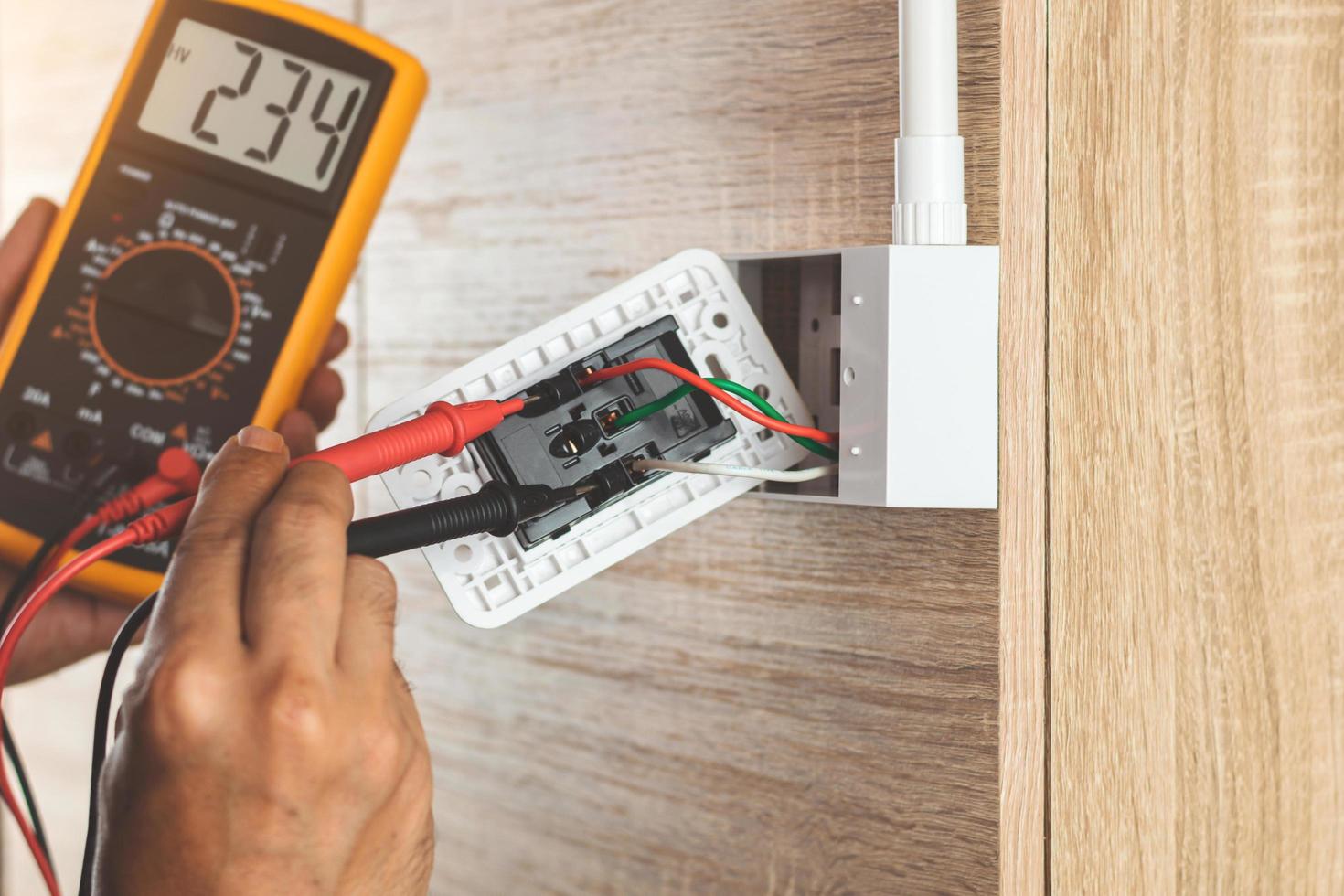 verwijder de elektrische stekker uit het stopcontact op de houten muur om de spanning te meten met een digitale meter. foto