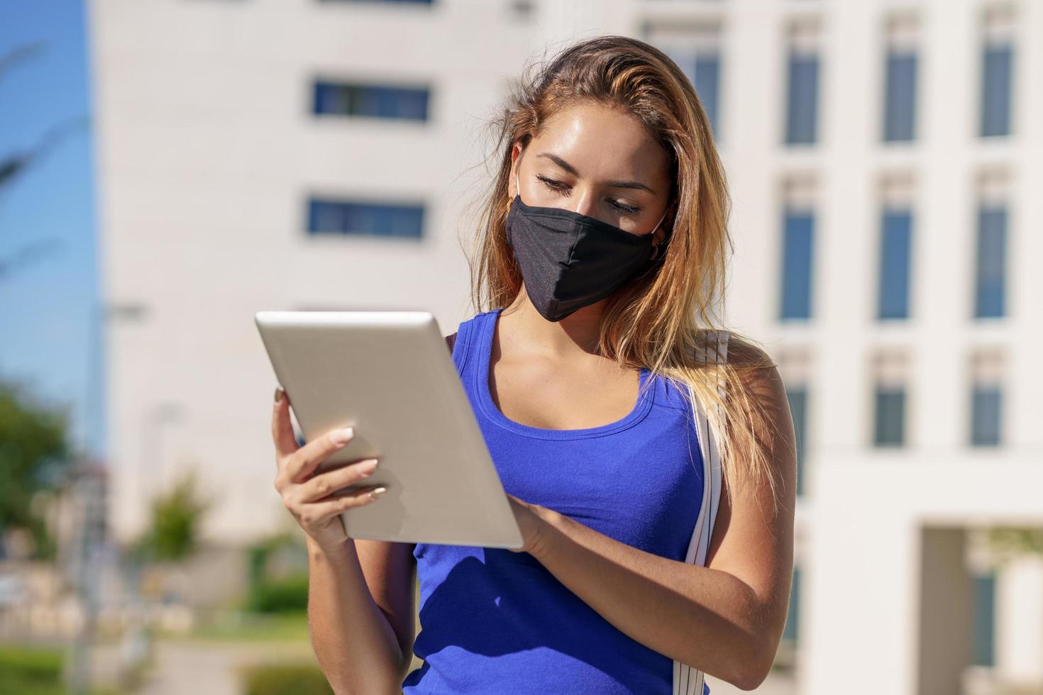 jonge vrouw die een masker draagt, gebruikt buitenshuis digitale tablet. foto