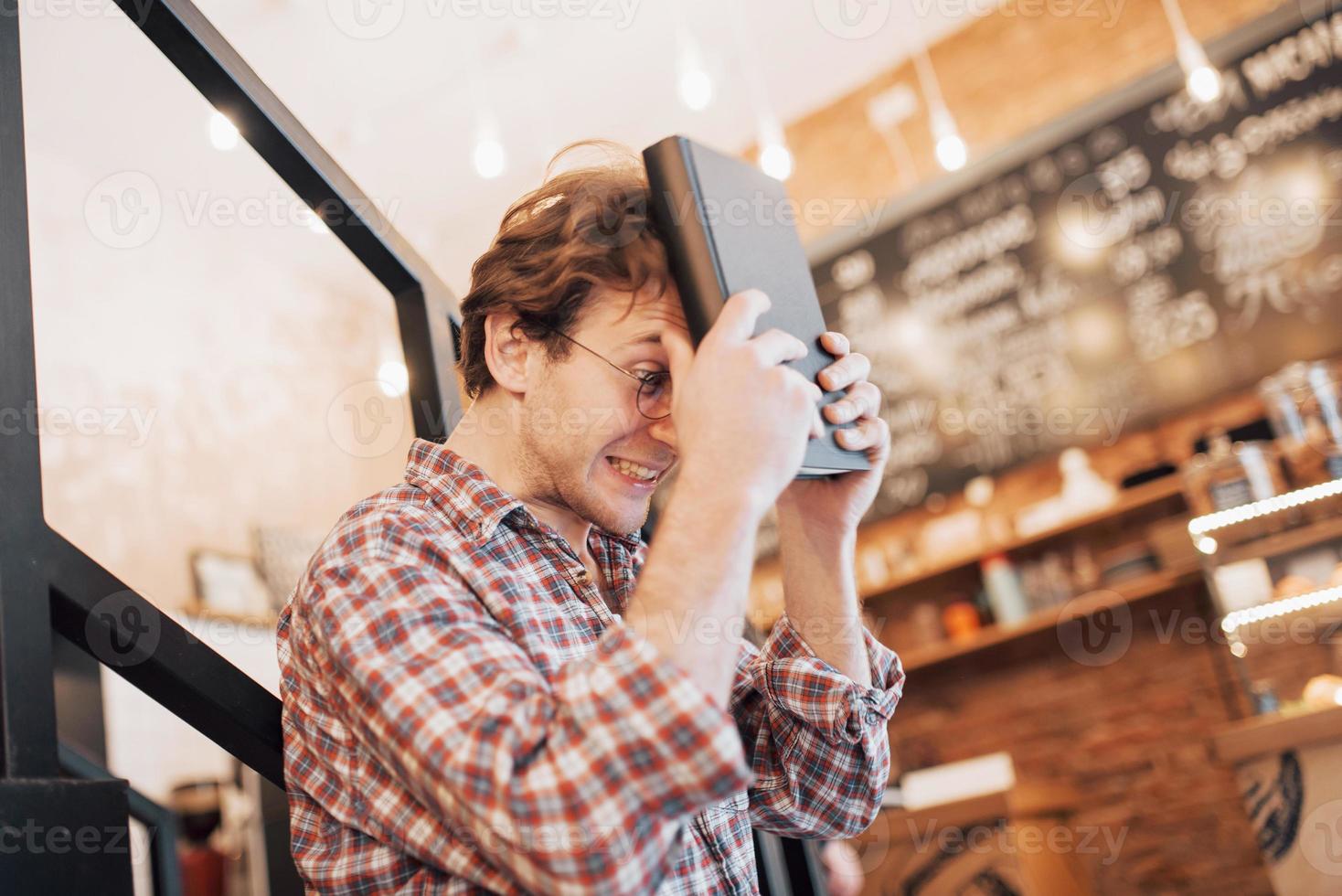 doordachte jongeman zit in de banketbakkerij. ze drinkt koffie terwijl ze op iemand wacht foto